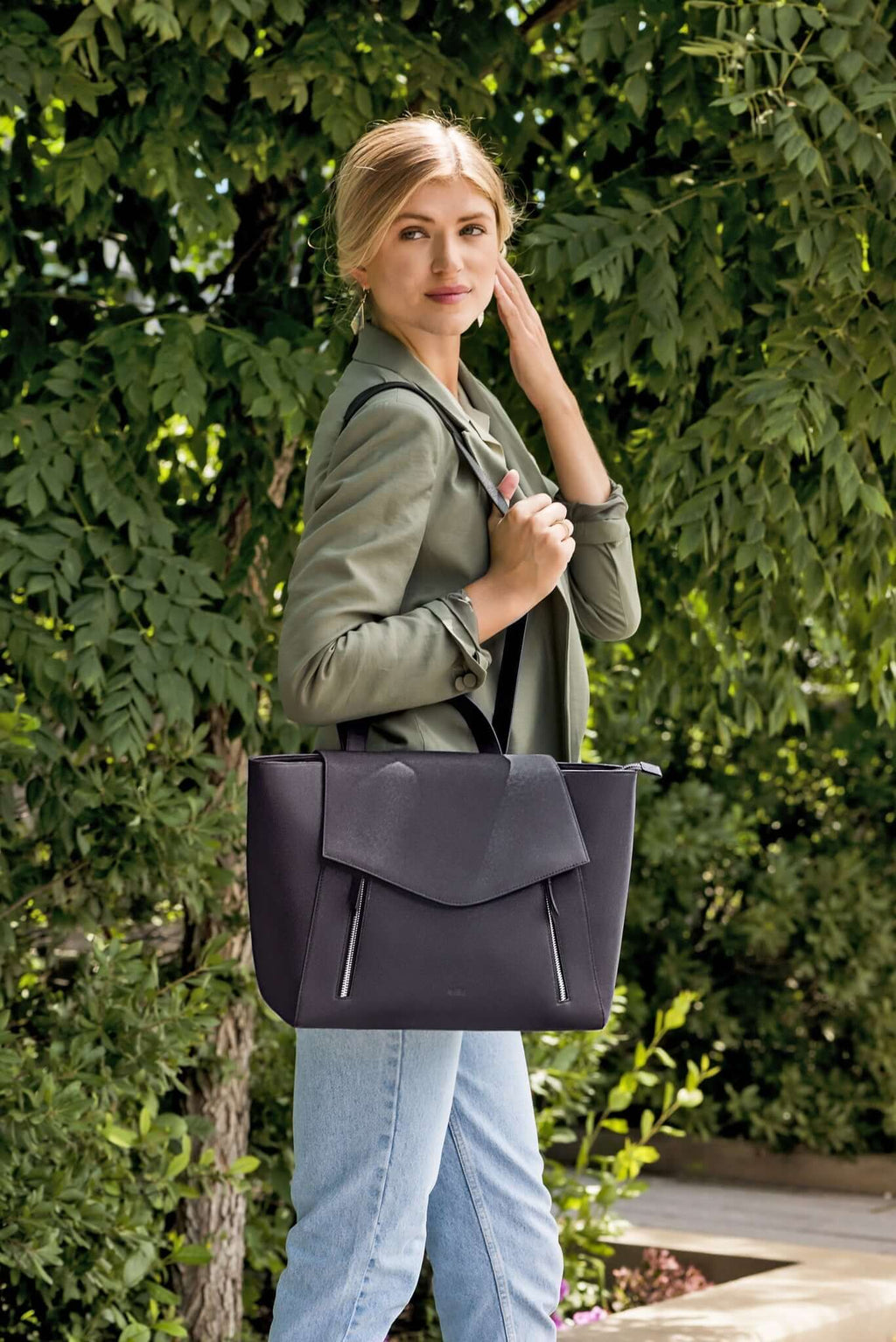 work bag for women. Woman wearing AGIKI convertible leather laptop work bag for women, styled as a shoulder bag in a garden setting.